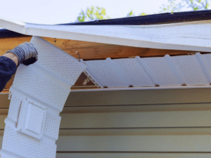 Person wearing a glove attaches a white perforated gutter section under the eaves of a house during installation.